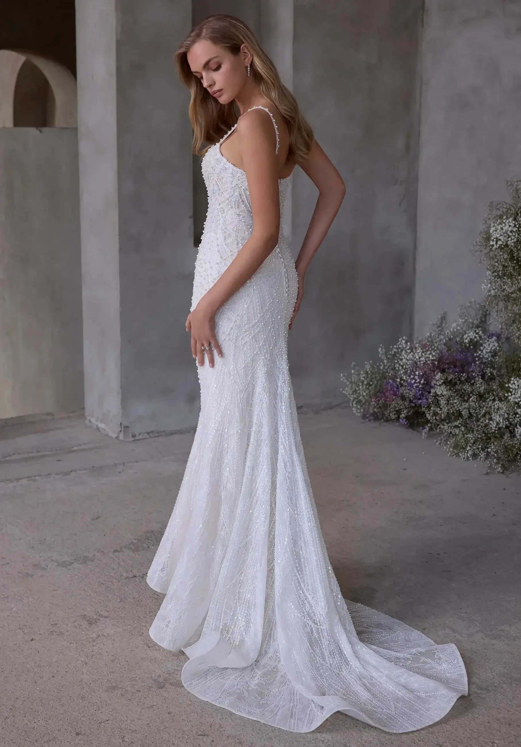 Model is wearing a fit-and-flare wedding dress with an angel wing neckline, thin straps, basque waist, and pearl-embroidered tulle.