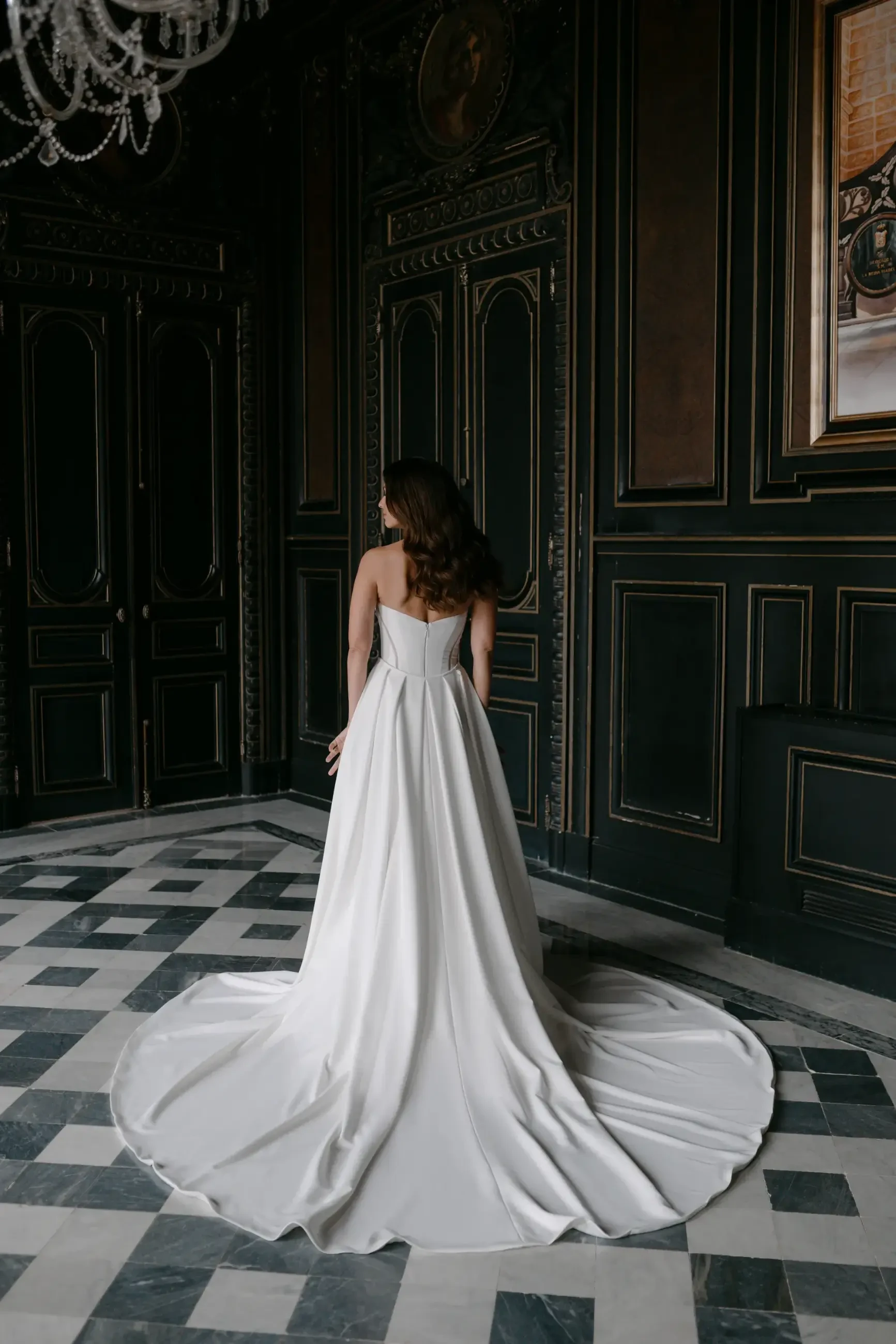 Model is wearing a floor-length, sheath-silhouette wedding gown in crepe with a cateye strapless neckline and basque waistline.