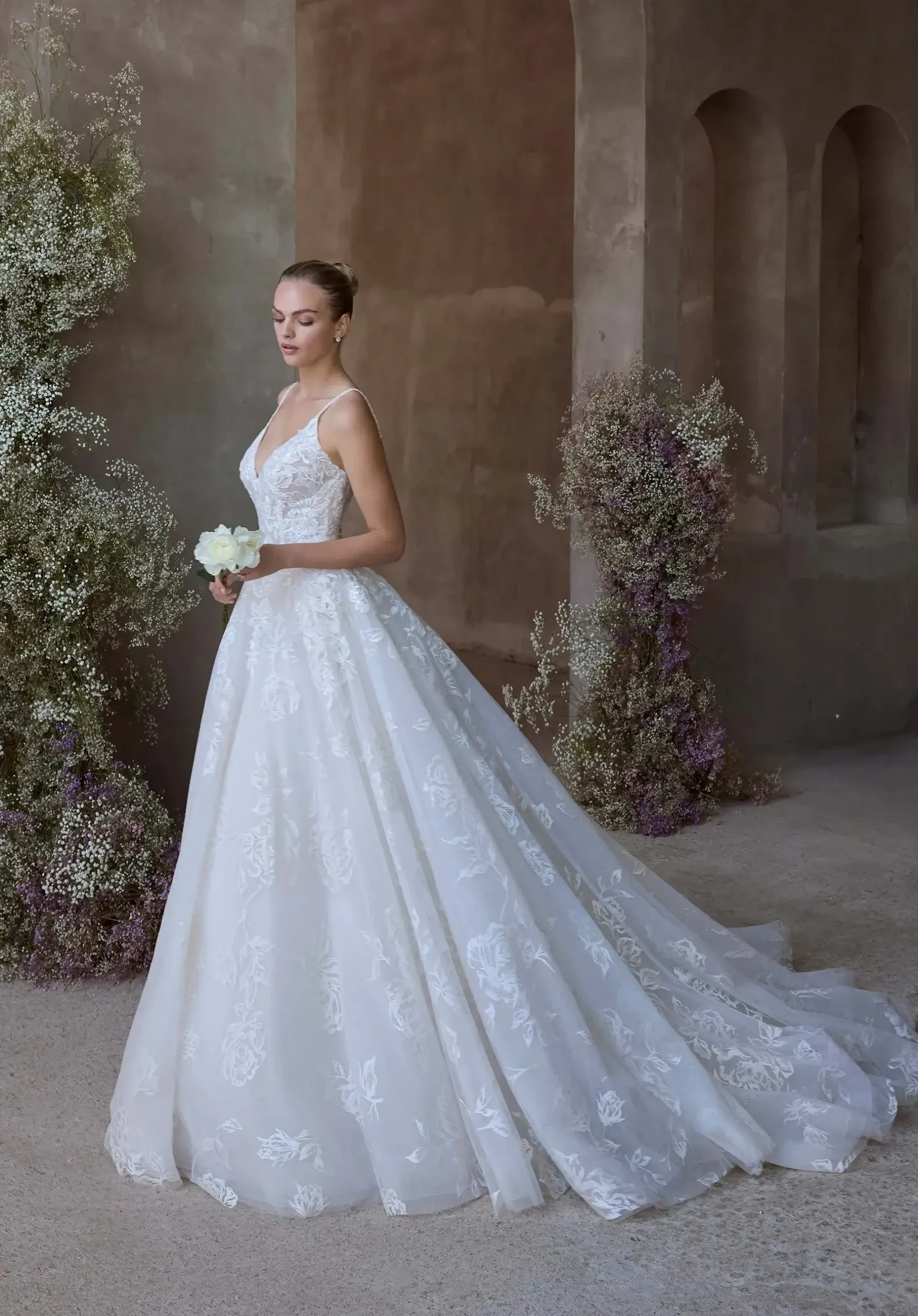 Model is wearing a ball gown wedding dress with a V-neckline, thin straps, rose-printed organza, and glitter tulle overlay.