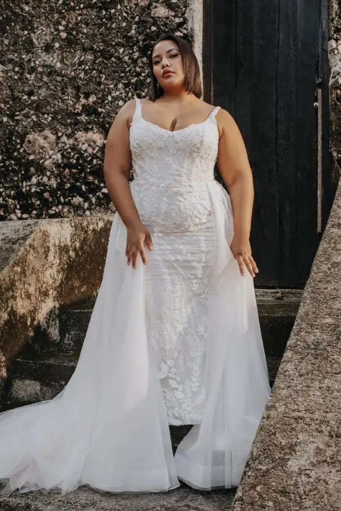 Model is wearing a wedding dress with pearlescent beading and a detachable tulle train
