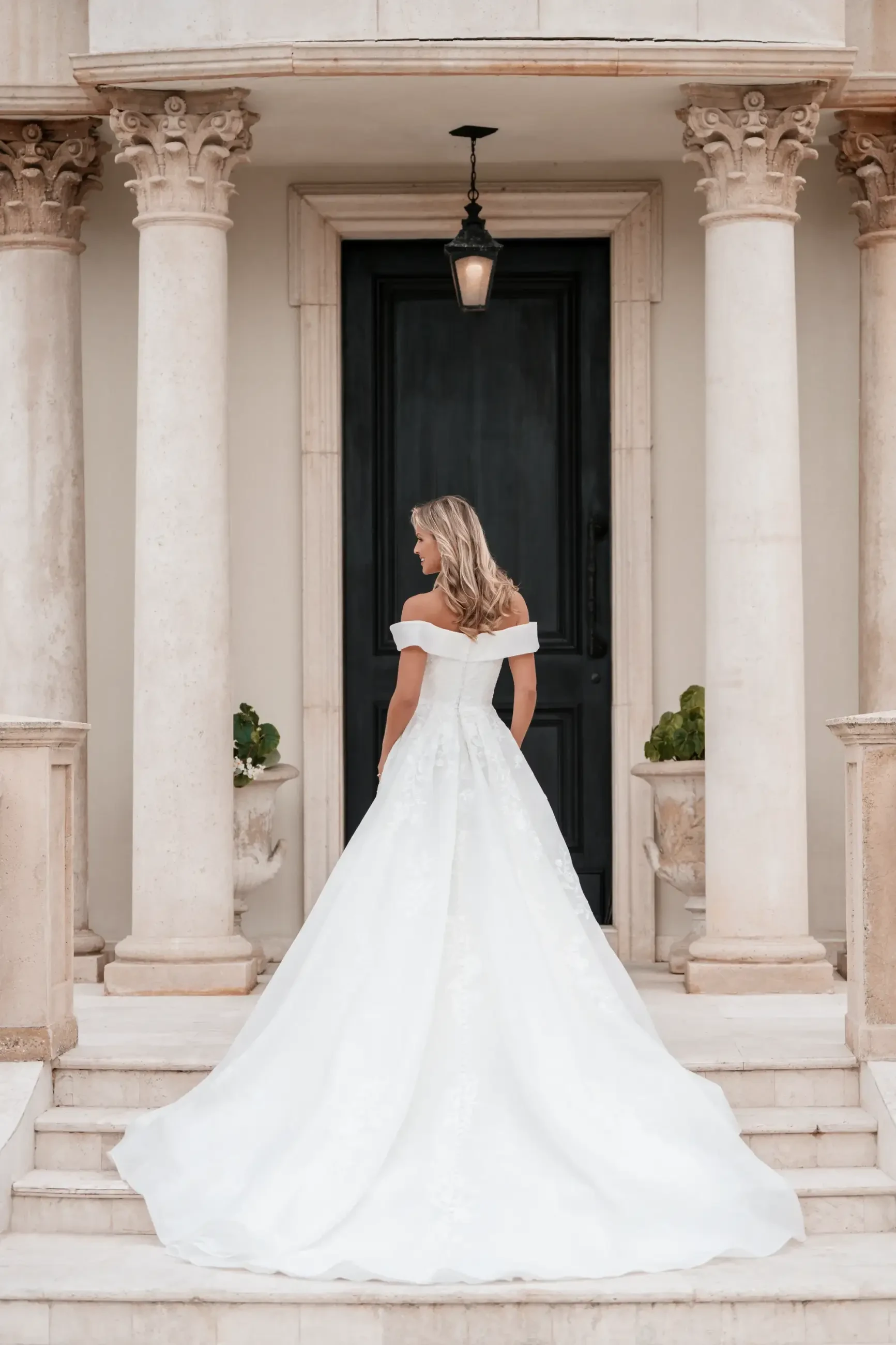 Model is wearing a ballgown wedding dress with a sweetheart neckline, off-the-shoulder organdy sleeves, sequin lace appliques, and a subtle slit.
