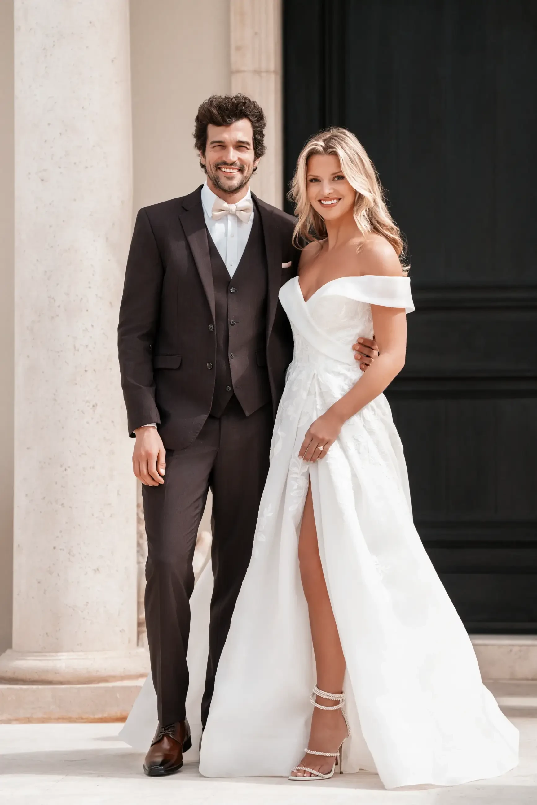 Model is wearing a ballgown wedding dress with a sweetheart neckline, off-the-shoulder organdy sleeves, sequin lace appliques, and a subtle slit.