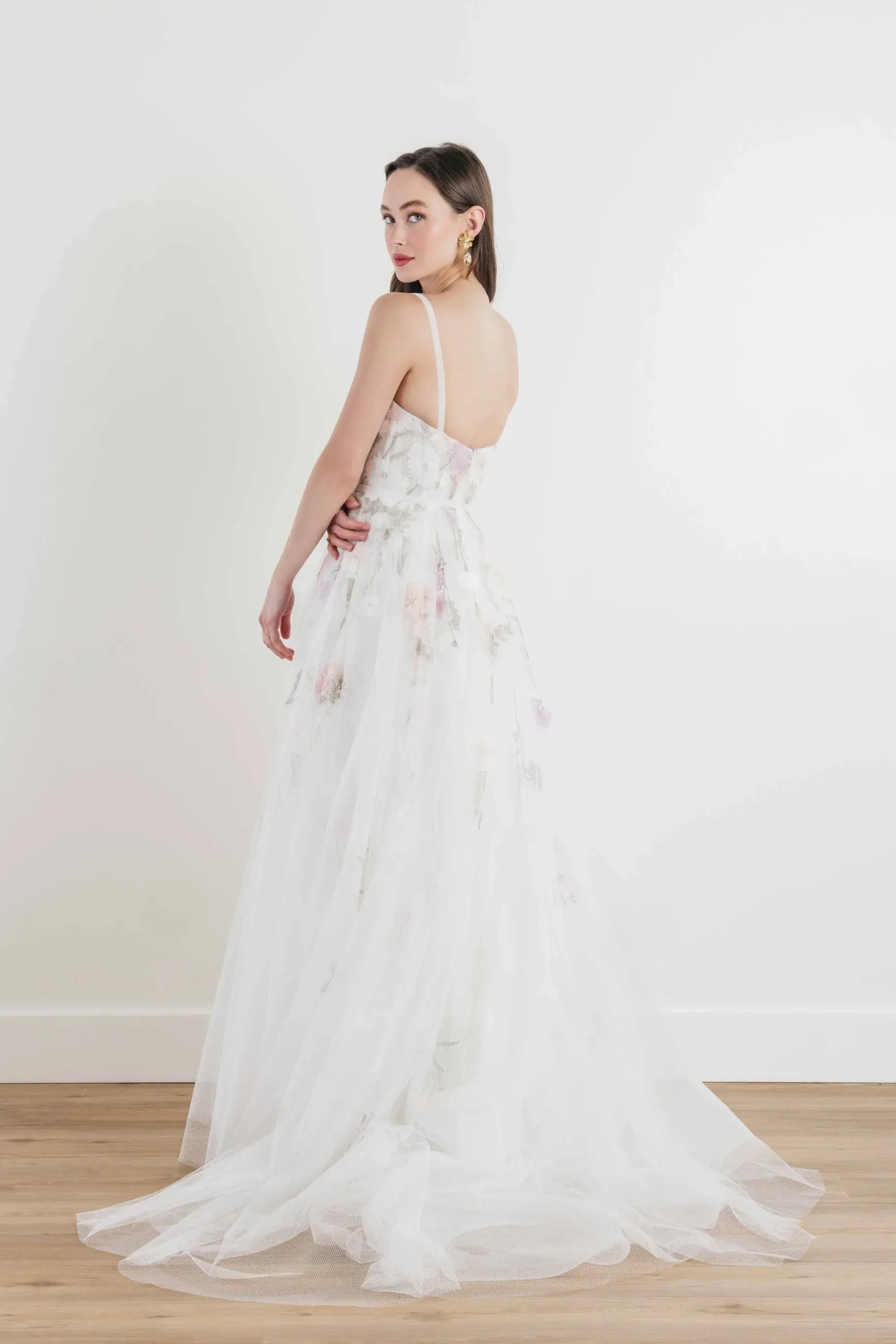 Model is wearing an a-line wedding dress with a sweetheart neckline and pastel floral accents