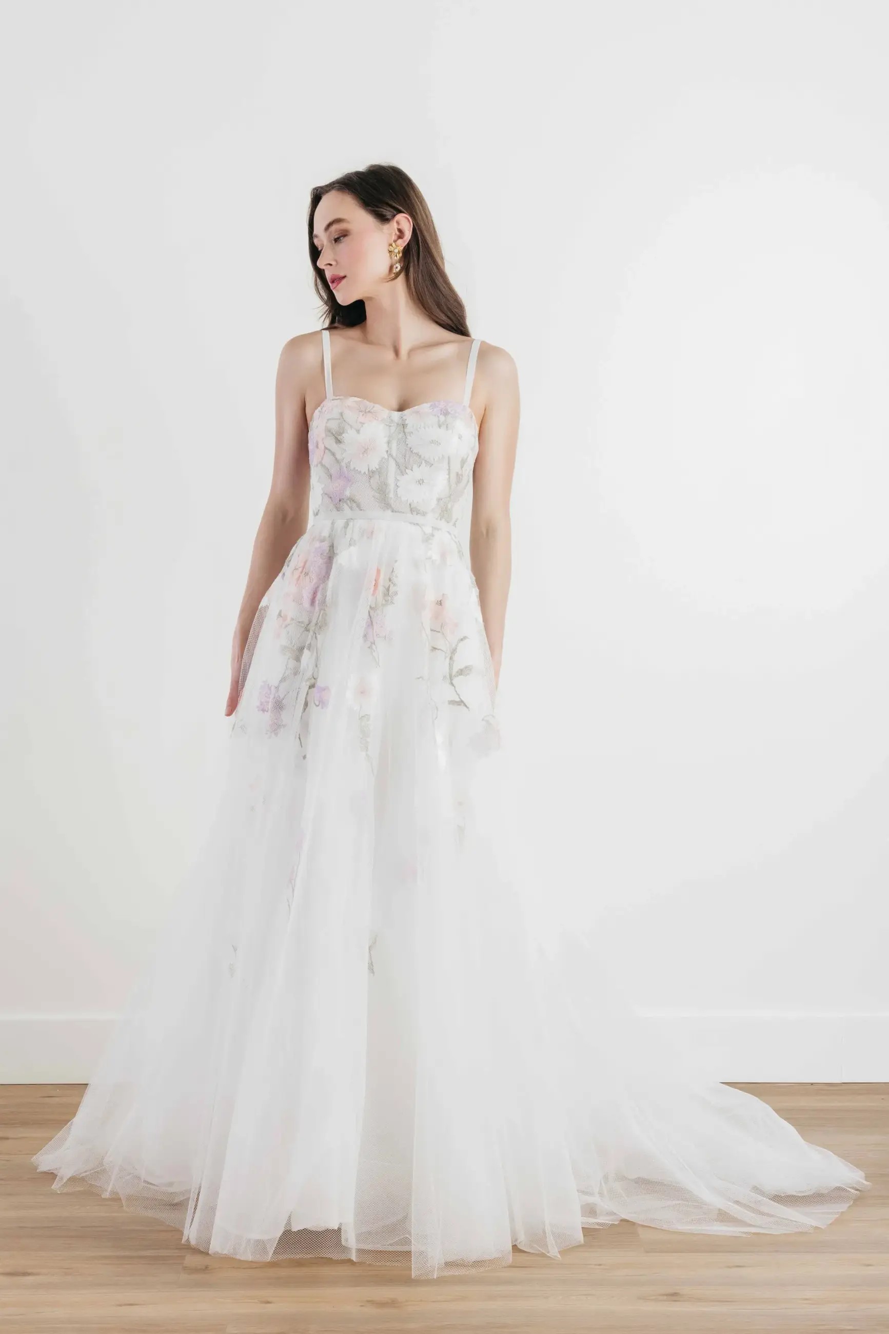 Model is wearing an a-line wedding dress with a sweetheart neckline and pastel floral accents