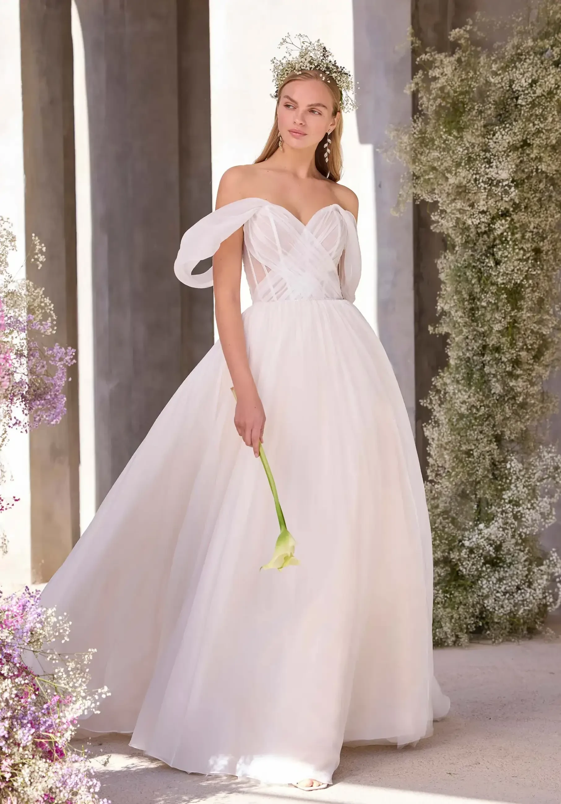 Model is wearing a strapless organza A-line gown with a sweetheart neckline, off-the-shoulder sleeves, and a sparkling beaded waistband.