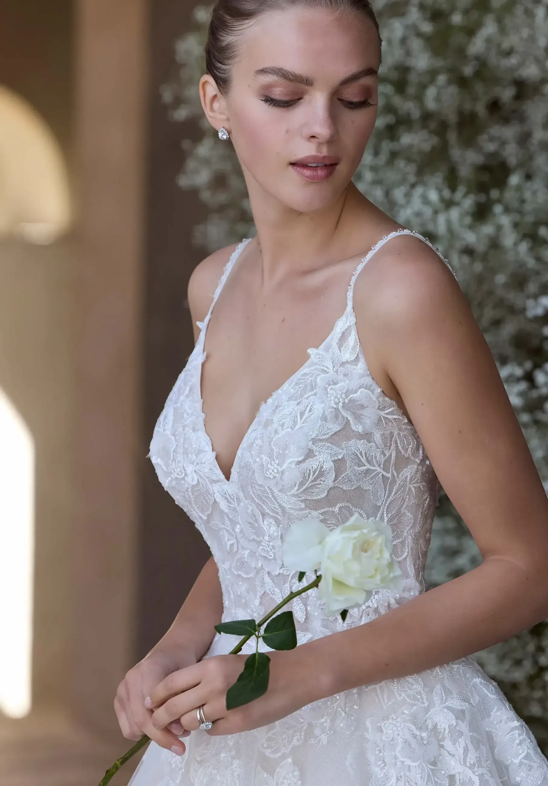 Model is wearing a ball gown with thin straps, a V-neckline, and rose-printed organza layered over glitter tulle.
