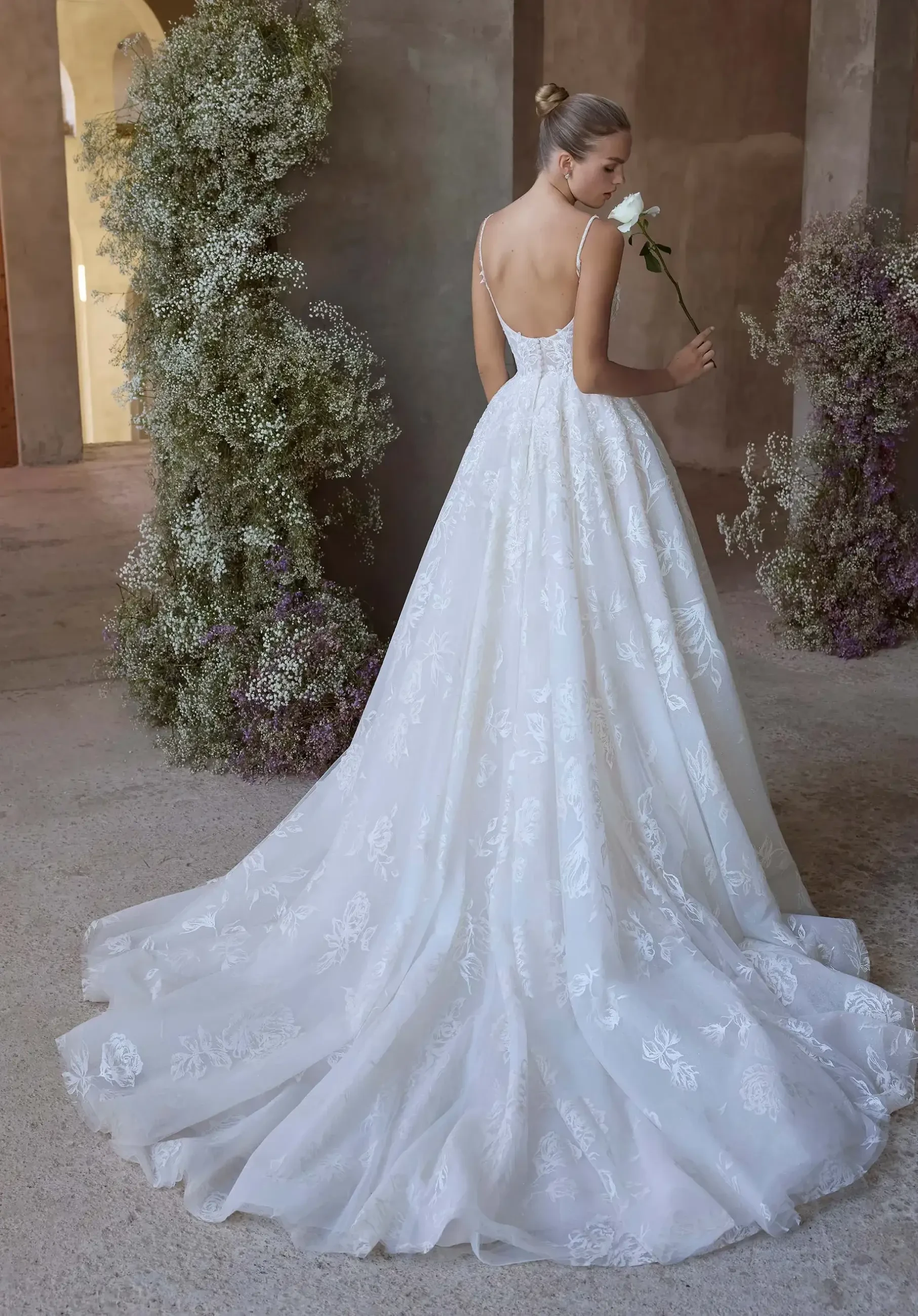 Model is wearing a ball gown with thin straps, a V-neckline, and rose-printed organza layered over glitter tulle.