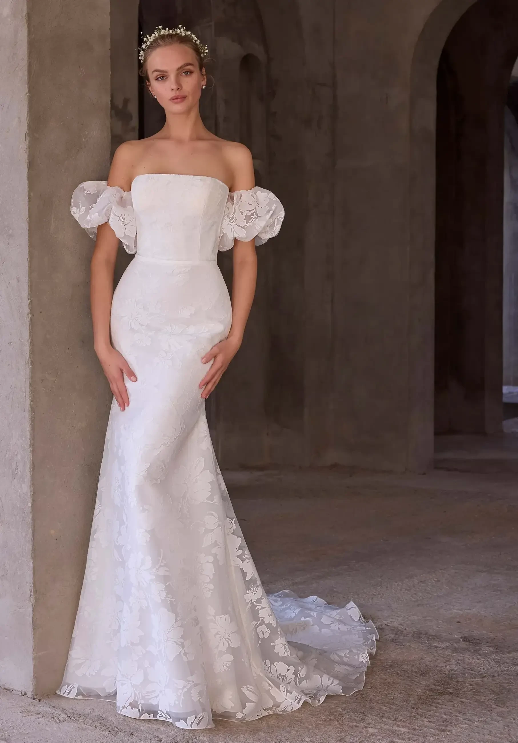 model is wearing an off the shoulder bridal gown with a watteau train