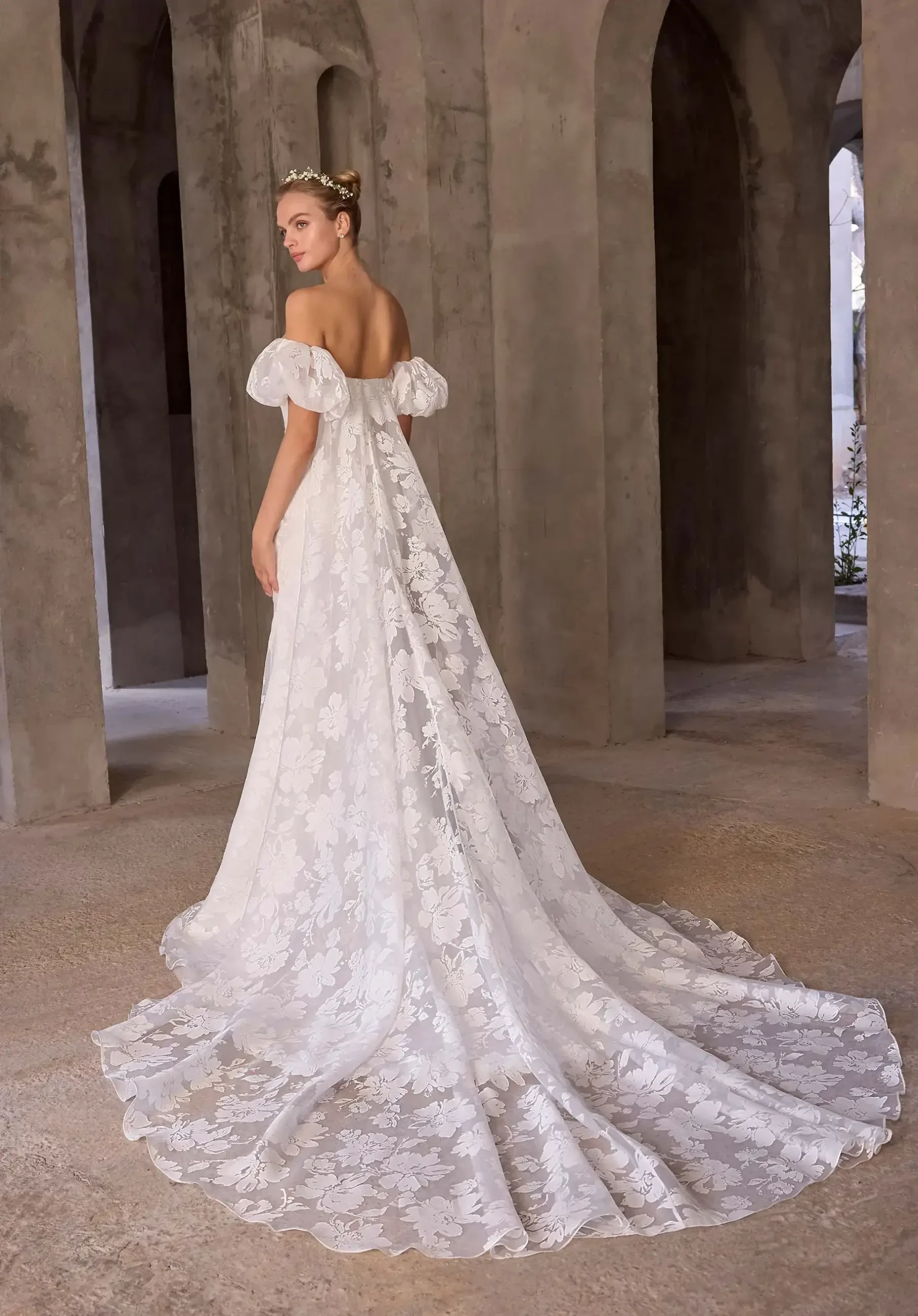 model is wearing an off the shoulder bridal gown with a watteau train